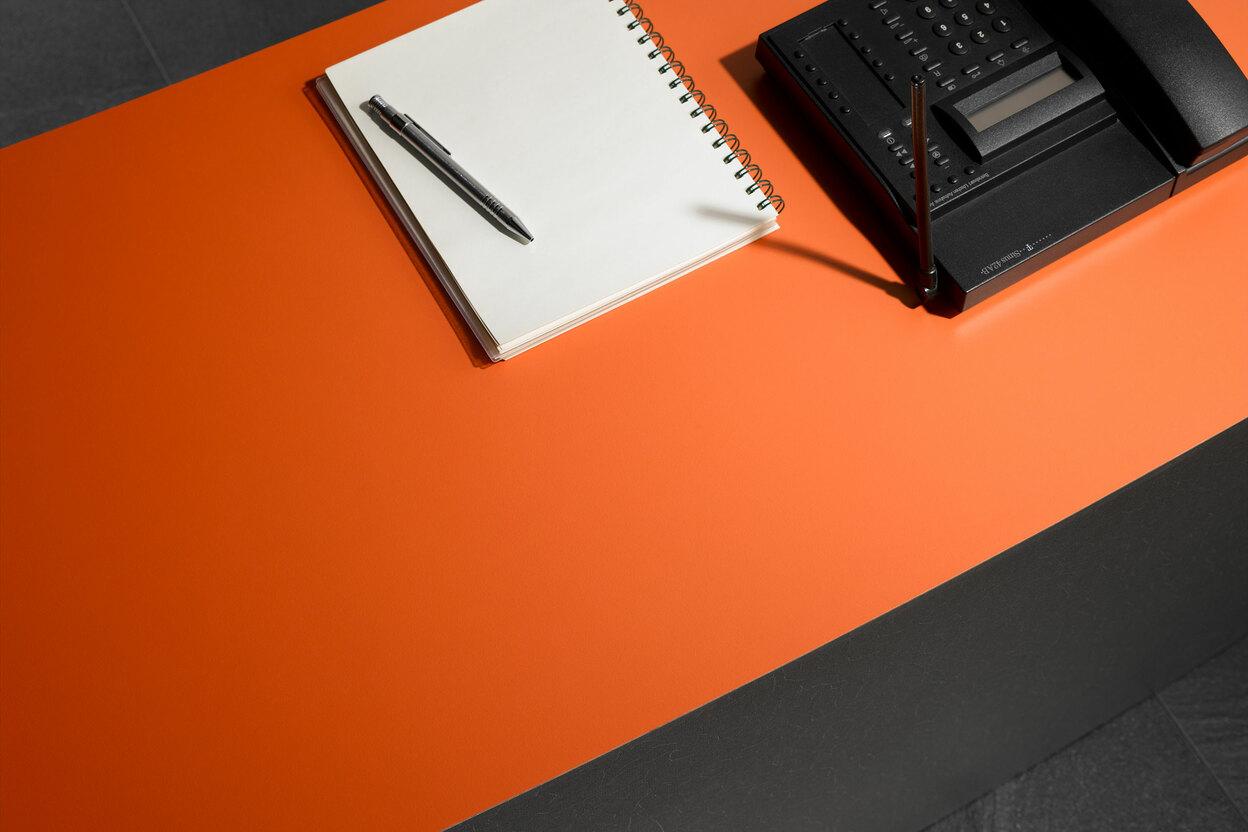 Detailaufnahme einer orangenen Arbeitsplatte mit dunkler Außenkante am Empfang
