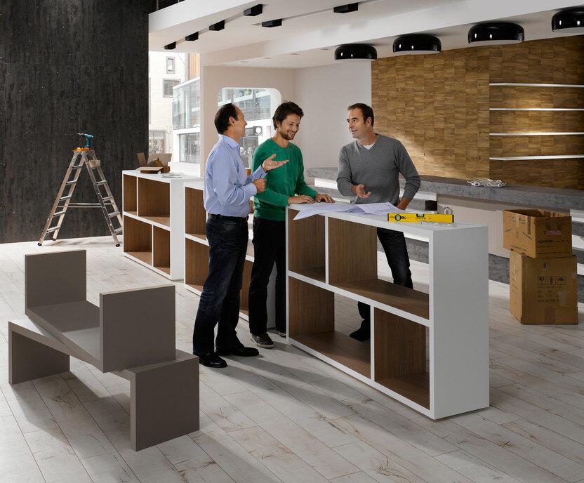 Planungsgespräch für Messe-/Showroomaufbau Planungsgespräch für Messe-/Showroomaufbau zwischen drei Männern mit unfertigen Mobiliar im Hintergrund